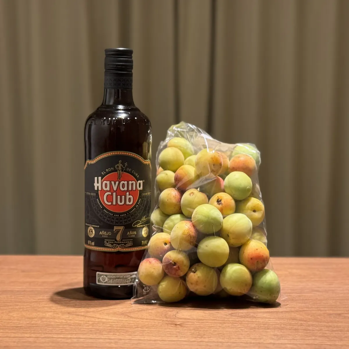 Green ume plums in a net bag next to a bottle of seven-year aged dark rum
