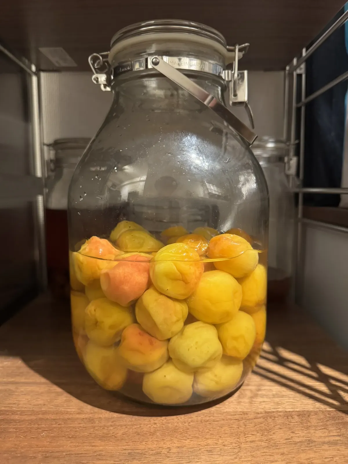 The jar with clear umezu brine risen to fully submerge the plums, which are now deep yellow and orange